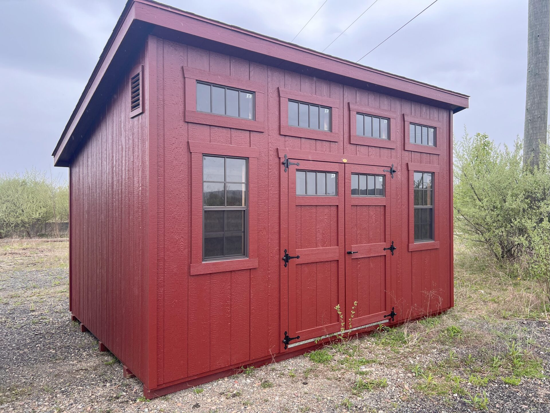 One slant red building with double doors, 2 windows and transom windows above