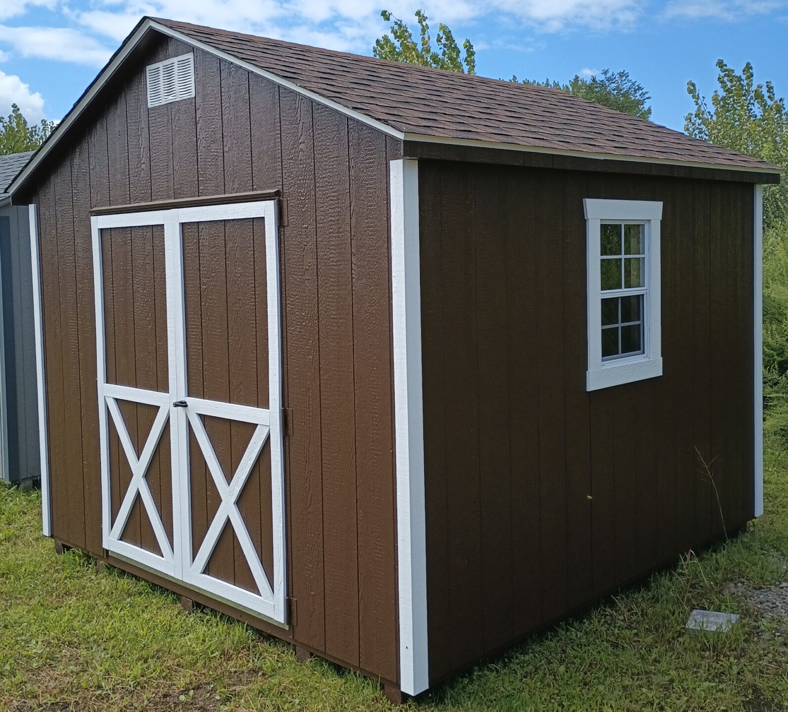 Brown shed with white trim, double doors, shingles and two windows